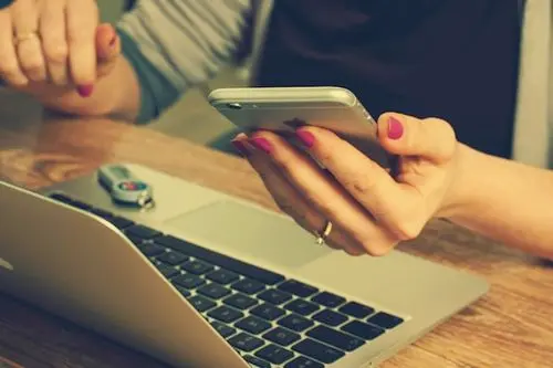 Person shopping on a phone next to an open laptop