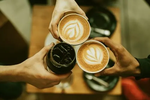 Three people holding takeaway coffee cups over a café table